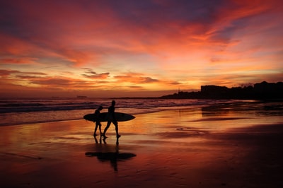 The man carrying a surfboard silhouette of the sunset
